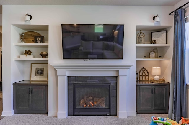 living area with baseboards, a glass covered fireplace, built in shelves, and carpet