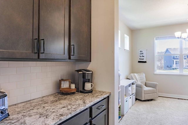 interior space with dark brown cabinetry, light stone countertops, light colored carpet, a chandelier, and tasteful backsplash