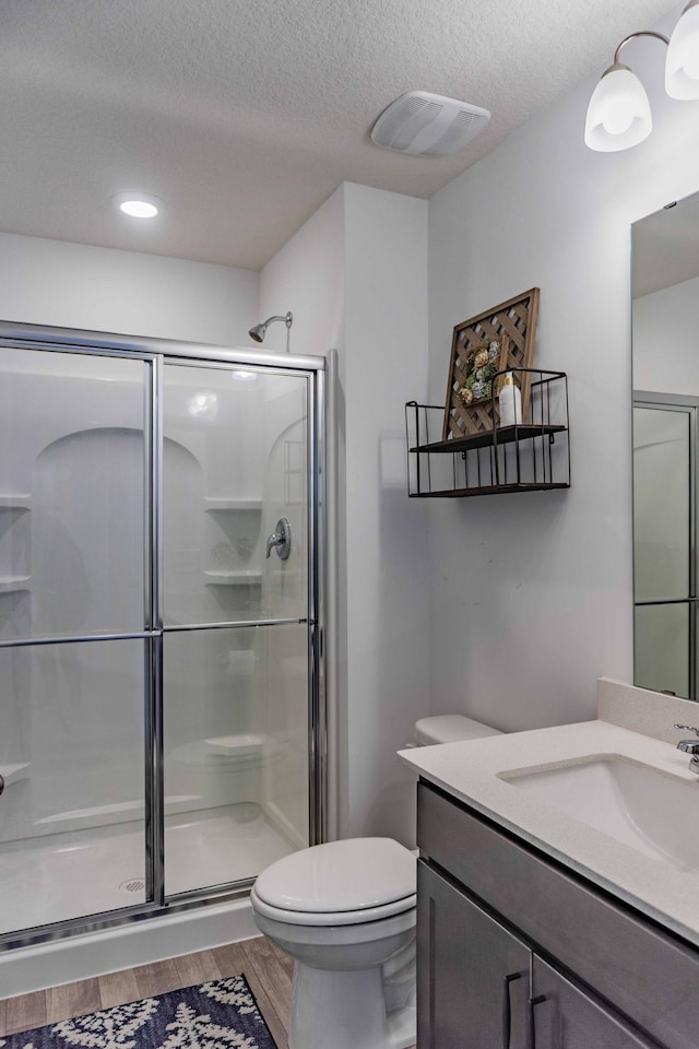 bathroom featuring vanity, toilet, a textured ceiling, a shower stall, and wood finished floors