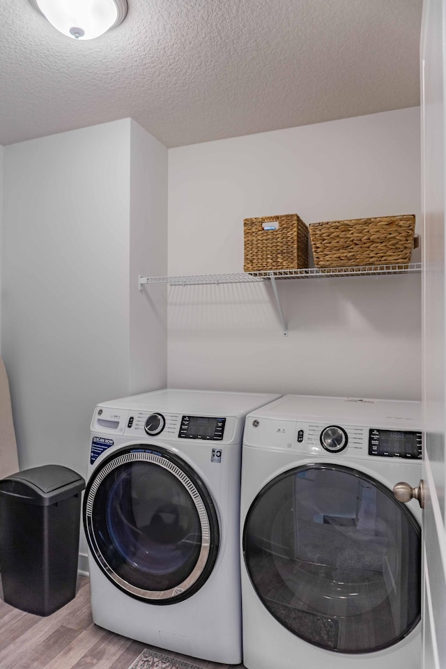 laundry area with washing machine and clothes dryer, a textured ceiling, laundry area, and wood finished floors
