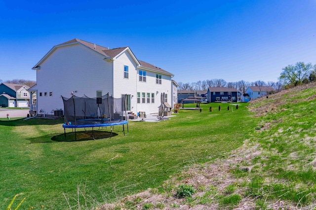 rear view of property with a yard, a patio, central AC, and a trampoline