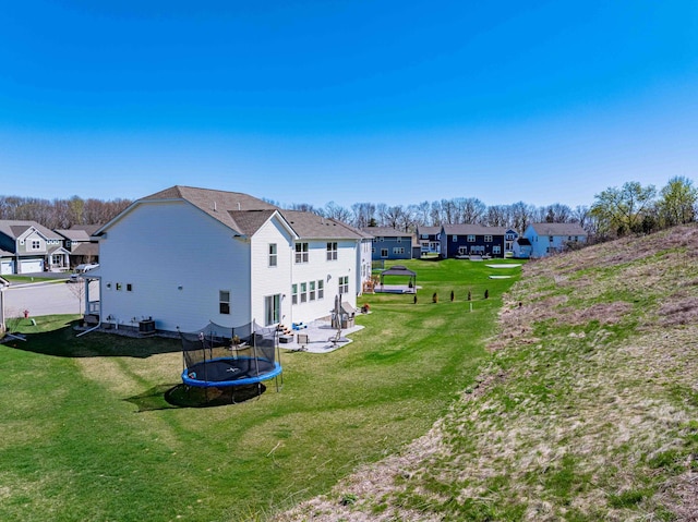 back of property featuring a lawn, a residential view, a patio area, and a trampoline