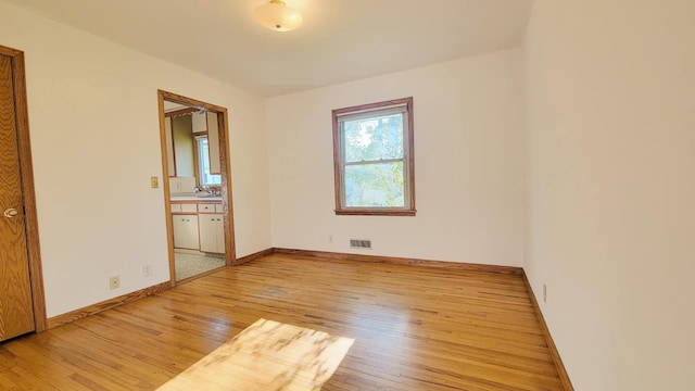 unfurnished bedroom featuring light wood-type flooring, baseboards, and ensuite bathroom