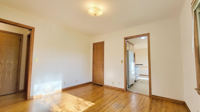 unfurnished bedroom featuring freestanding refrigerator, light wood finished floors, and baseboards
