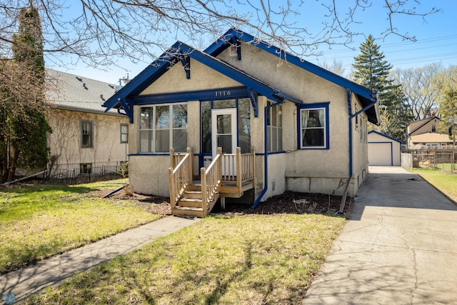 bungalow featuring fence, a front lawn, a detached garage, stucco siding, and an outbuilding