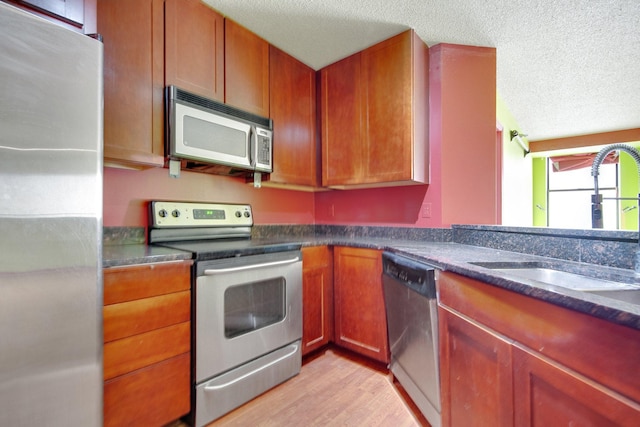 401 1st St Unit 401, Minneapolis, MN 55401 - kitchen with appliances with stainless steel finishes, a textured ceiling, a sink, light wood finished floors, and brown cabinets
