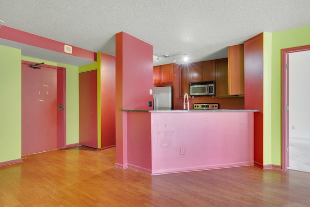 401 1st St Unit 401, Minneapolis, MN 55401 - kitchen featuring appliances with stainless steel finishes, track lighting, light wood-type flooring, a peninsula, and a textured ceiling