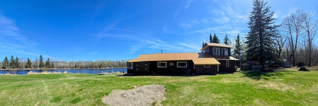 rear view of house featuring a water view, a lawn, and metal roof
