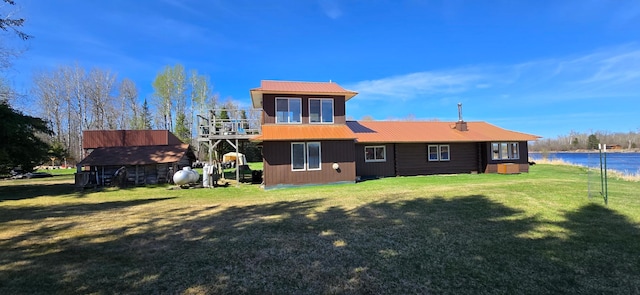back of house featuring a lawn, metal roof, an outbuilding, and a water view