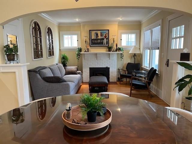 living area with crown molding, arched walkways, wood finished floors, and a fireplace