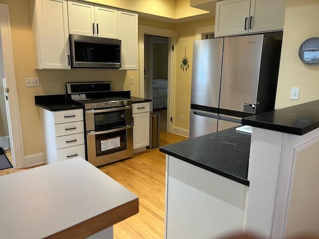 kitchen with dark countertops, appliances with stainless steel finishes, white cabinetry, a peninsula, and light wood-style flooring