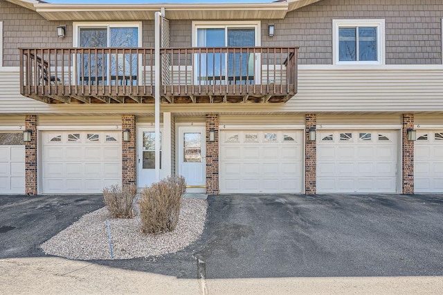 townhome / multi-family property featuring brick siding, an attached garage, driveway, and a balcony
