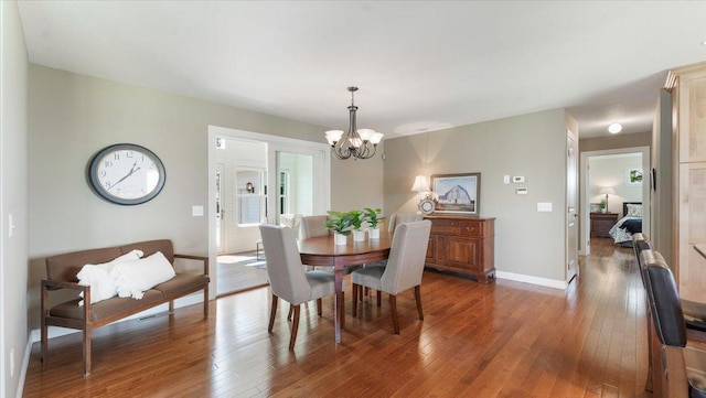 dining space with baseboards, a notable chandelier, and hardwood / wood-style flooring