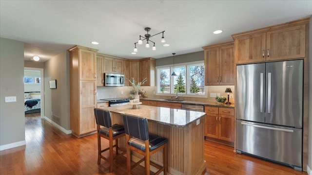 kitchen with decorative backsplash, wood finished floors, a sink, light stone counters, and stainless steel appliances