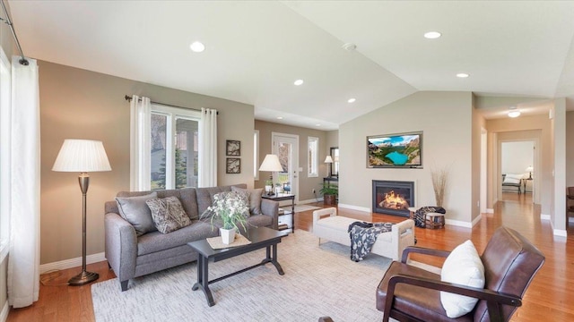 living area with a glass covered fireplace, lofted ceiling, baseboards, recessed lighting, and light wood finished floors