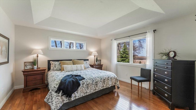 bedroom featuring a tray ceiling, baseboards, and wood finished floors