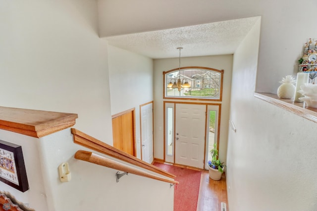 entryway featuring an inviting chandelier, a textured ceiling, and wood finished floors