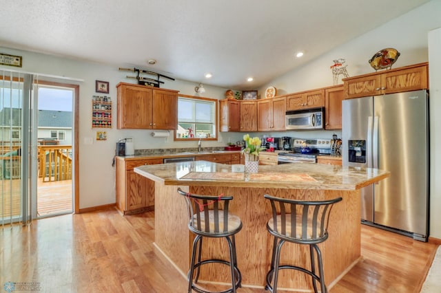 kitchen with a sink, light wood finished floors, stainless steel appliances, a kitchen bar, and a kitchen island