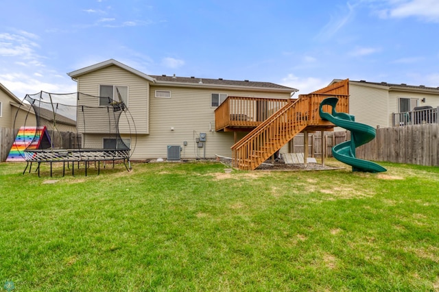 rear view of property featuring a trampoline, fence, cooling unit, a playground, and a yard