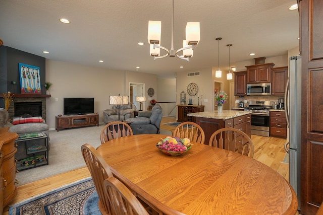 dining area with a notable chandelier, a fireplace, recessed lighting, light wood-type flooring, and visible vents
