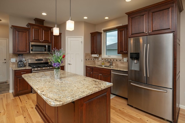 kitchen featuring backsplash, appliances with stainless steel finishes, a sink, and light wood-type flooring