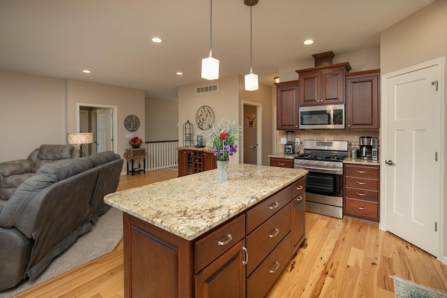 kitchen with visible vents, hanging light fixtures, open floor plan, stainless steel appliances, and light wood-style flooring