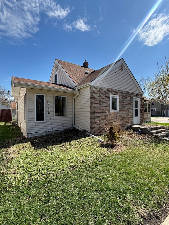 rear view of property featuring a lawn, a chimney, and stone siding