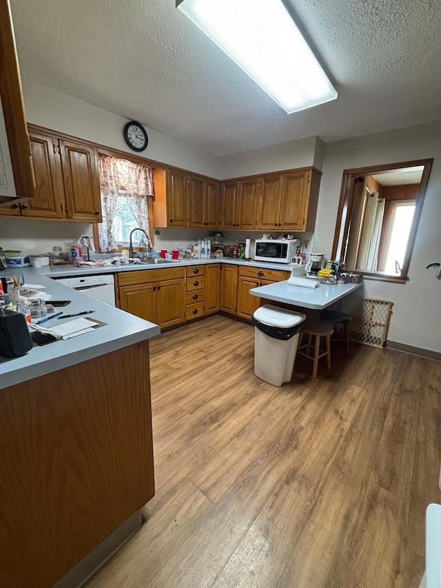 kitchen with light countertops, a textured ceiling, white appliances, and light wood-style flooring