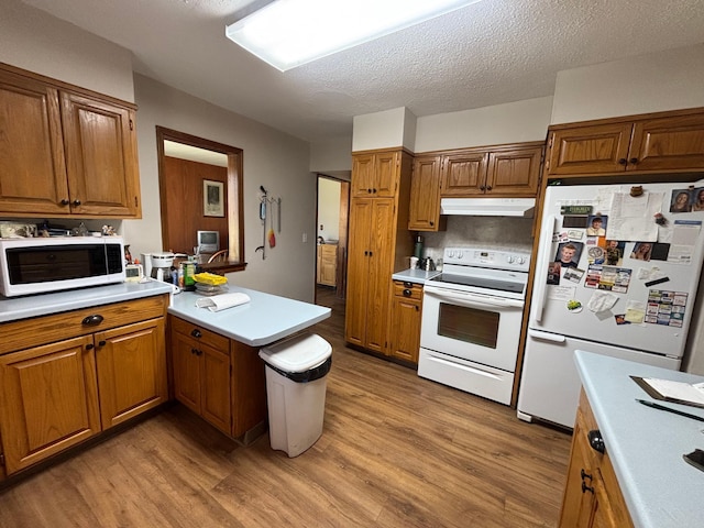kitchen with a peninsula, white appliances, light countertops, under cabinet range hood, and light wood-style flooring