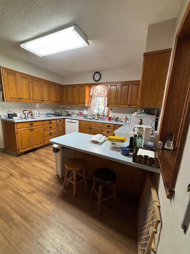 kitchen featuring brown cabinetry, a peninsula, white dishwasher, a textured ceiling, and light wood finished floors