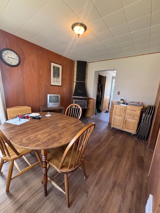 dining space featuring a wood stove, wood walls, and dark wood-type flooring