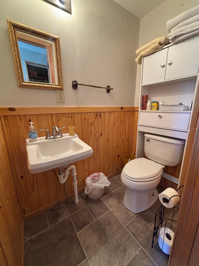 bathroom with wood walls, a sink, a wainscoted wall, and toilet