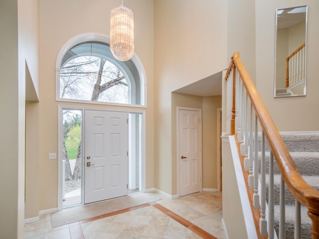 foyer with stairway, a chandelier, a high ceiling, and baseboards