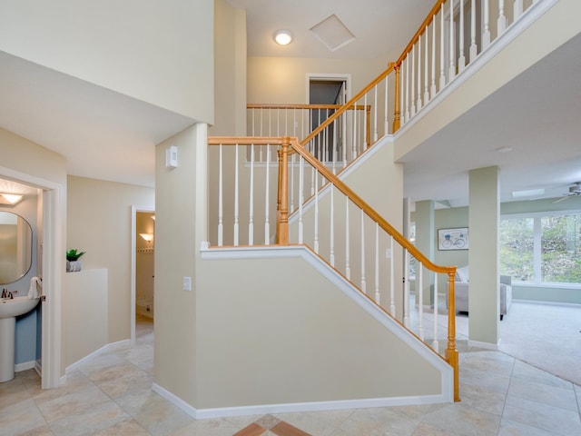 staircase featuring baseboards, ceiling fan, and a towering ceiling