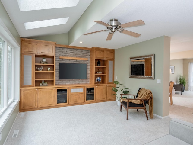living room with a ceiling fan, vaulted ceiling with skylight, visible vents, baseboards, and light carpet