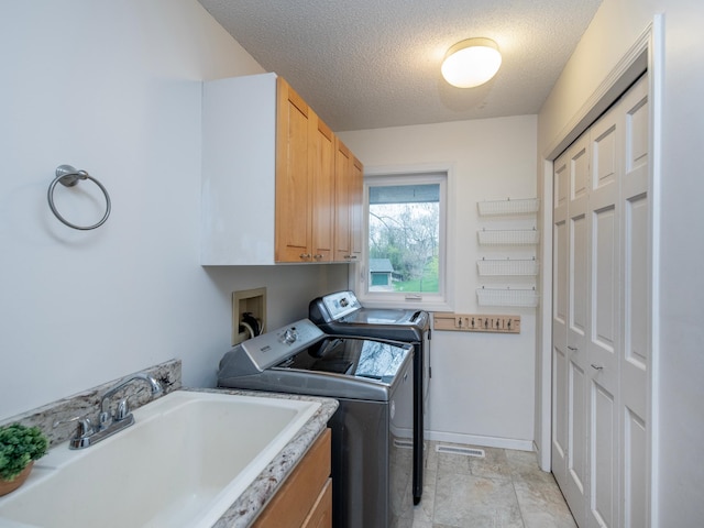 washroom with washing machine and dryer, a textured ceiling, baseboards, a sink, and cabinet space