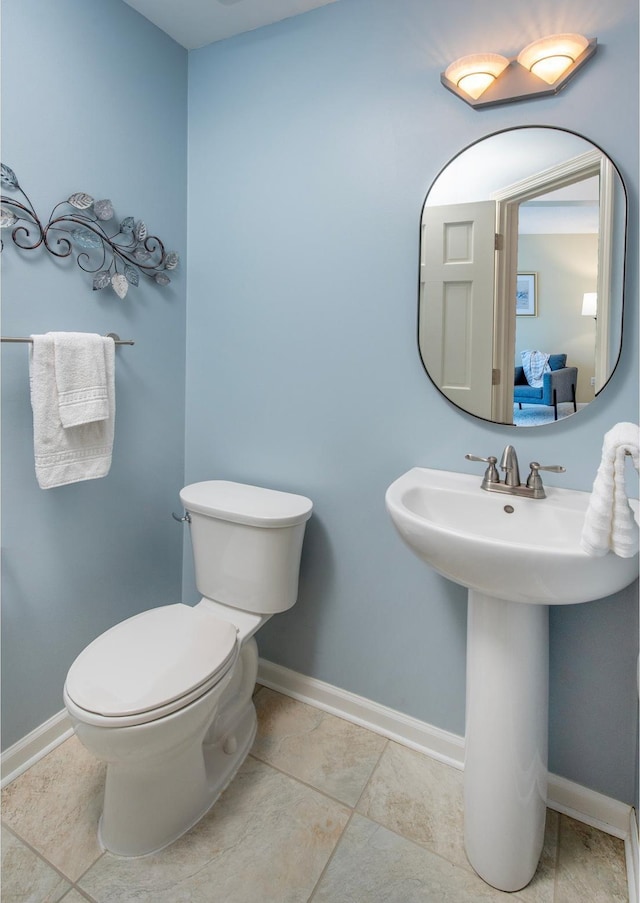 half bath featuring toilet, baseboards, tile patterned flooring, and a sink