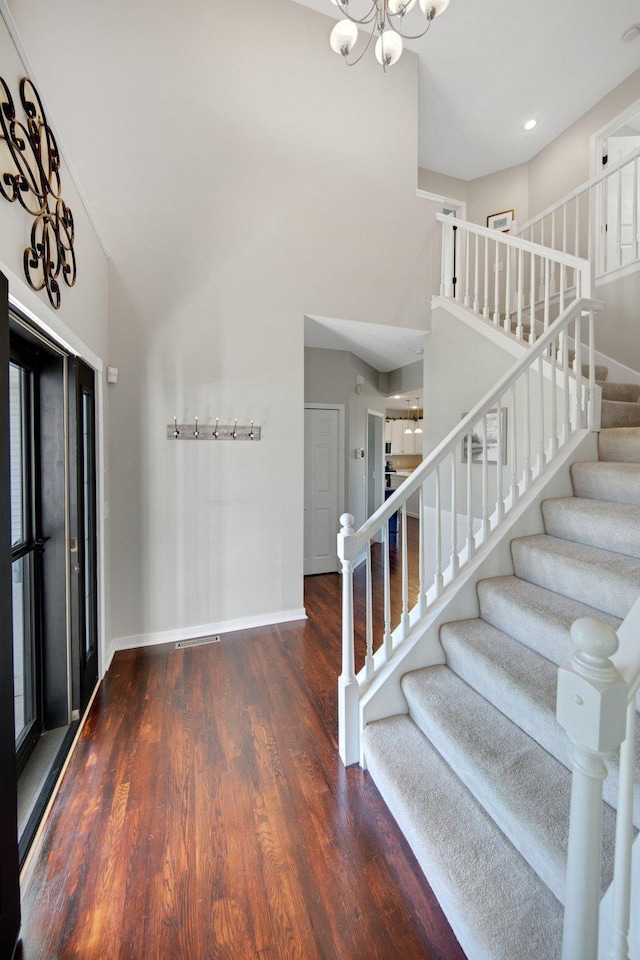 staircase featuring a towering ceiling, wood finished floors, baseboards, an inviting chandelier, and recessed lighting