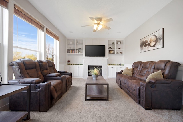 living room with ceiling fan, built in shelves, light carpet, and a fireplace