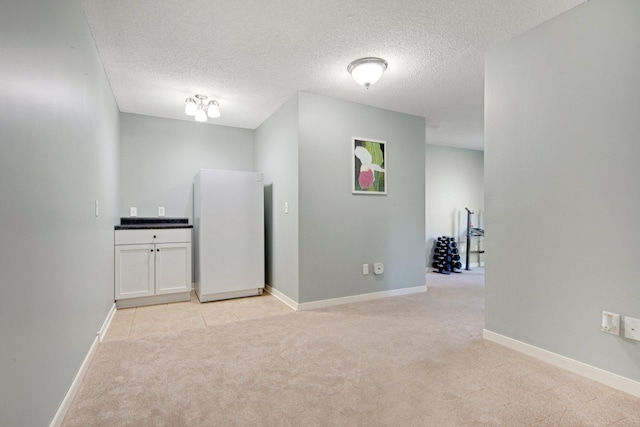 empty room featuring baseboards, a textured ceiling, and light colored carpet