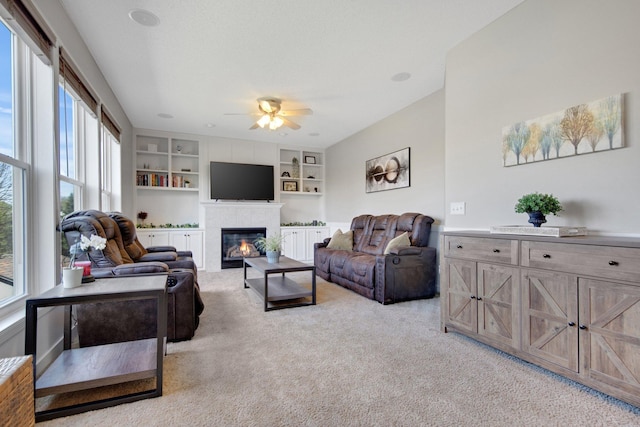 living room with built in shelves, light carpet, a ceiling fan, and a tile fireplace