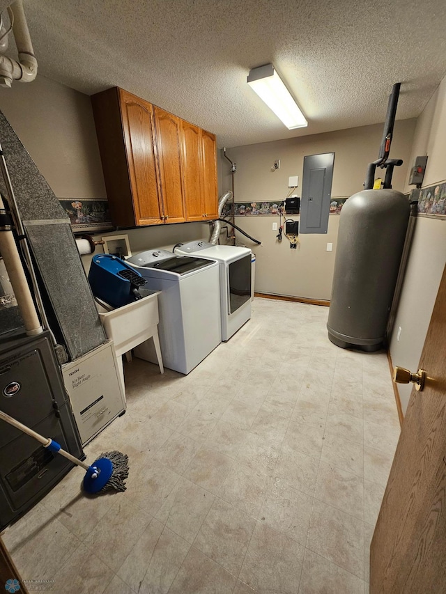 washroom featuring cabinet space, gas water heater, a textured ceiling, washer and clothes dryer, and electric panel