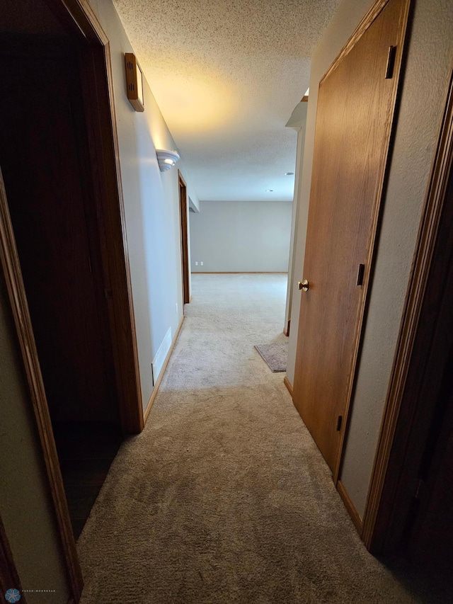 hallway with light colored carpet, a textured ceiling, and baseboards
