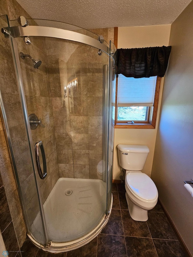 bathroom with toilet, a textured ceiling, tile patterned floors, baseboards, and a stall shower