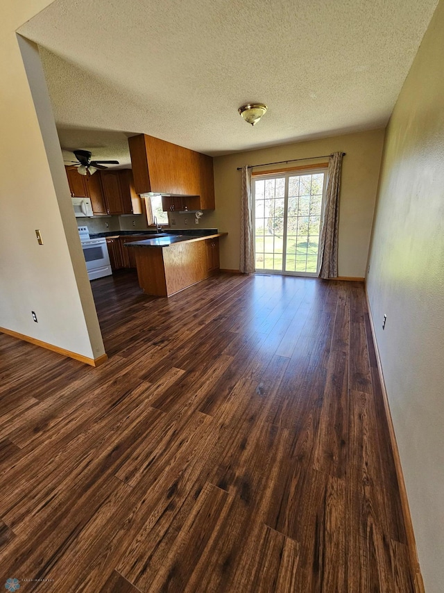 kitchen featuring a textured ceiling, dark wood finished floors, a peninsula, open floor plan, and white appliances