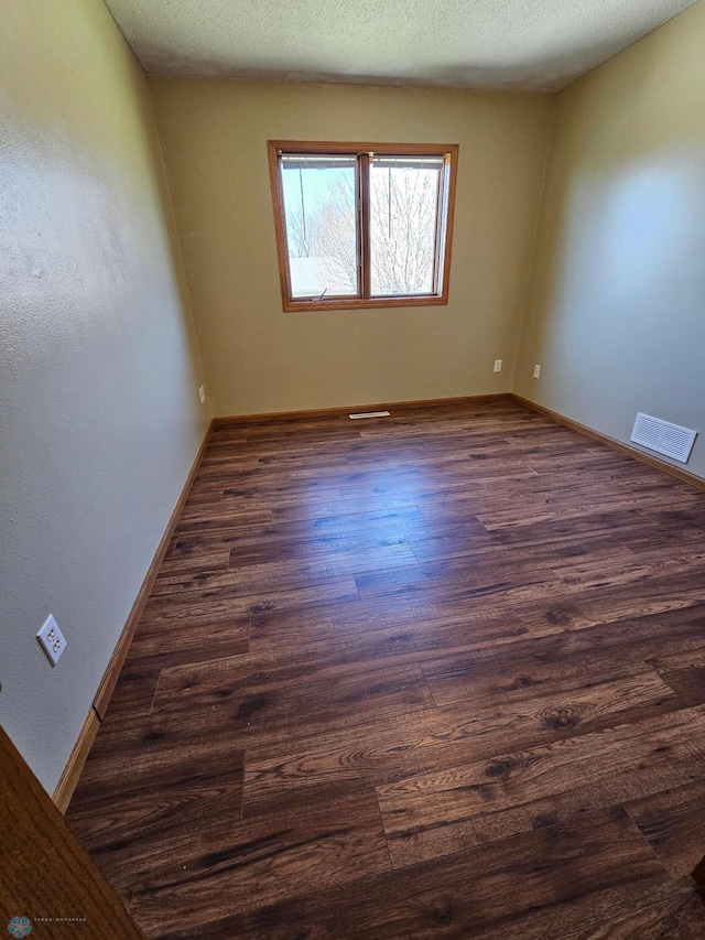unfurnished room featuring baseboards, dark wood finished floors, and visible vents