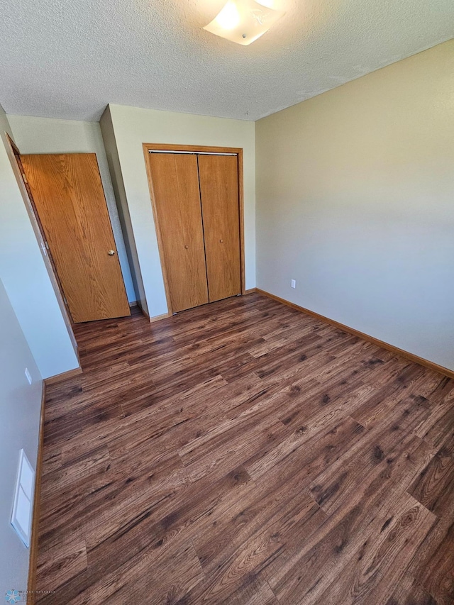 unfurnished bedroom with a textured ceiling, baseboards, dark wood-type flooring, and a closet