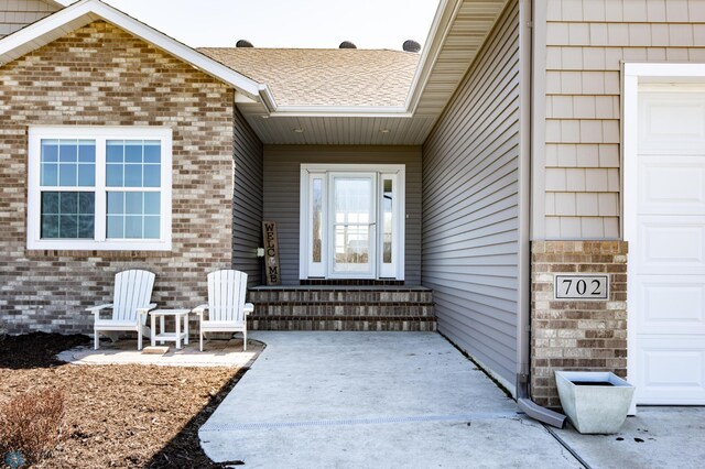 doorway to property featuring roof with shingles and brick siding