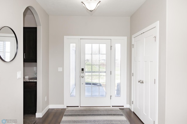 entrance foyer with baseboards, arched walkways, and dark wood finished floors