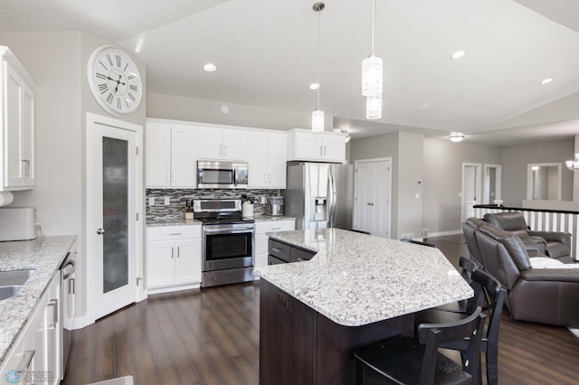 kitchen featuring appliances with stainless steel finishes, vaulted ceiling, open floor plan, dark wood-type flooring, and a center island
